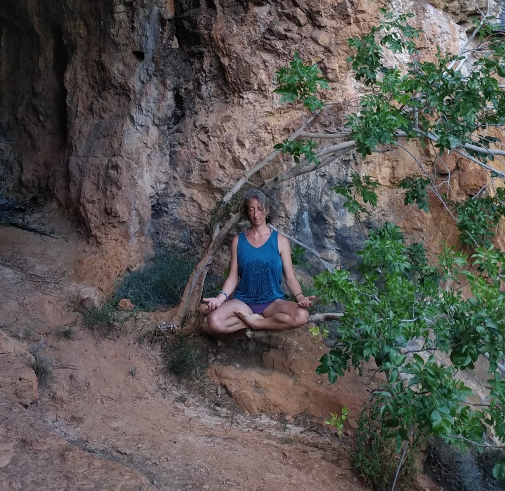 Anouk assise en posture de méditation au pied d’une falaise, sous un figuier