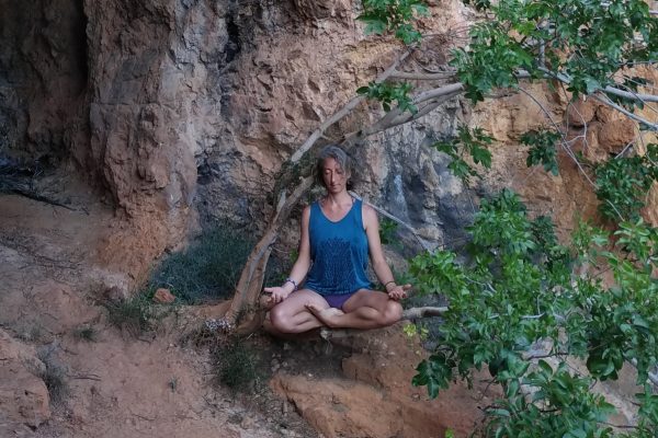 Anouk assise en posture de méditation au pied d’une falaise, sous un figuier